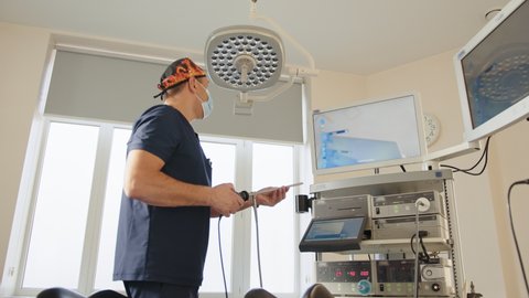 Portrait of a focused doctor holding a laparoscopic instrument, looking at the monitor and then at the camera. Use of laparoscopic equipment. Preparation for laparoscopy. Surgeon in operating room.