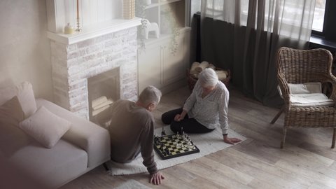 Top view. Elderly couple playing chess at home by the fireplace. Happy old age