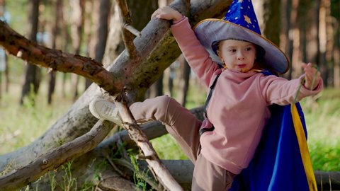 Girl, kid, plays in wizard costume in spring in forest, studies dry tree. Child in wizard's robe in spring in forest. Kid play magician outdoors. Halloween. Childhood, family. Child playing in park