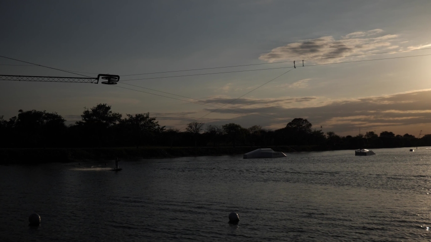 Camera pans with a wake boarder as he waterskis around the Ski Rixen lake at Quiet Waters Park, Deerfield Beach, Florida in slow-motion back-lit by the setting sun Royalty-Free Stock Footage #1088728209