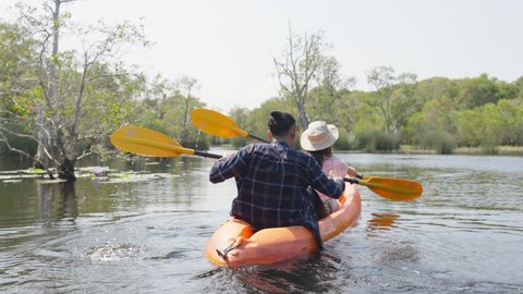 Asian attractive romantic young couple rowing kayak in a forest lake. Backpacker man and woman travel and kayaking on canoe in beautiful mangrove forest enjoy spend time on holiday vacation together.
