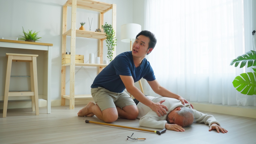 Asian young son helping senior male from falling on the ground at home. Elderly older mature grandfather having an accident after doing physical therapy then rescued by attractive man in living room. | Shutterstock HD Video #1088728499