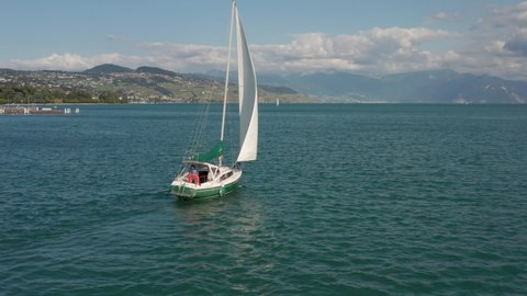 Beautiful aerial of boat sailing over lake Geneva and slowly revealing a large city in the background