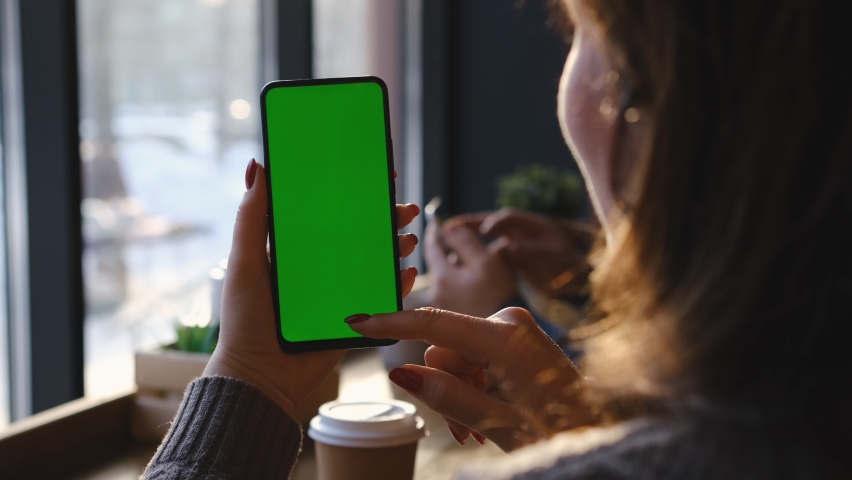 Woman is Holding Smartphone with Green Screen in cafe. Woman Hand. Cup of Hot coffee and Using Smartphone Watching Green Screen Top View. Smartphone with Green Mock-up Screen Business Concept. Royalty-Free Stock Footage #1088731501