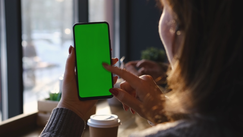 Woman is Holding Smartphone with Green Screen in cafe. Woman Hand. Cup of Hot coffee and Using Smartphone Watching Green Screen Top View. Smartphone with Green Mock-up Screen Business Concept. | Shutterstock HD Video #1088731501