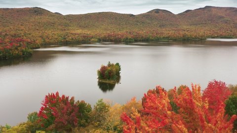 Breathtaking aerial view of mountain lake in Vermont Maine with Fall colors in peak season, USA 4K aerial on cloudy autumn day. Stunning red, orange and yellow tree tops in pure forest at scenic lake