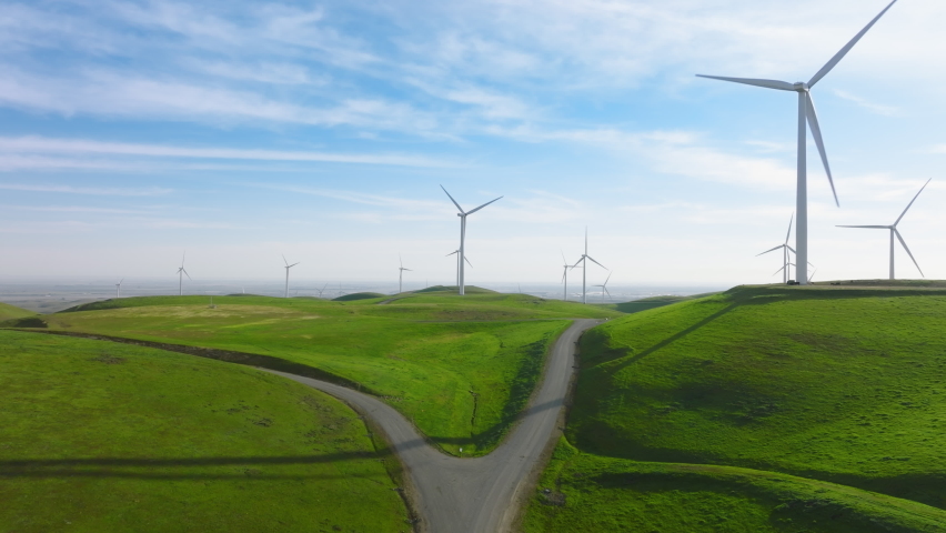 Windmill park green energy from drone view, windmill wind farm on green hills with rotating large windmill turbines generating renewable energy from the wind. High quality 4k footage, California USA