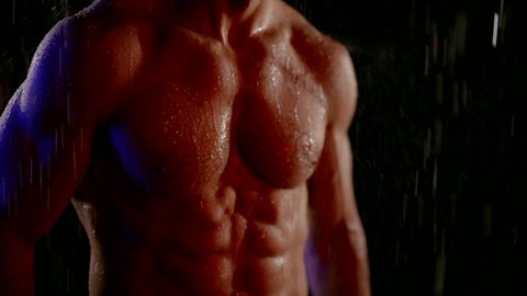 close-up of a muscular naked male torso under water drops on a dark background