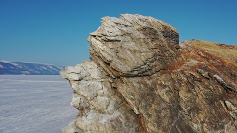 Aerial around view of frozen Lake Baikal, Ogoy Island, Dragon Tooth rock cape. Siberia, Russia, 4k
