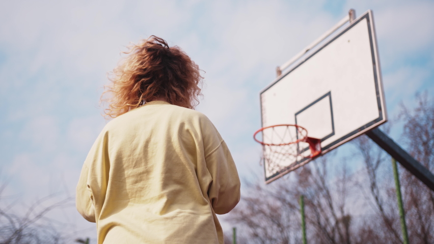 Teenage caucasian girl celebrating, jumping for joy with arms raised at basketball court. Success concept. Slow motion low angle
