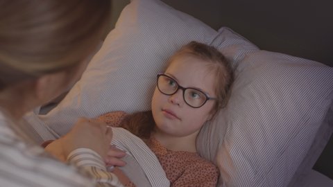 Slowmo shot of loving mother taking care of sick 11-year-old daughter lying in bed, measuring her temperature with electronic thermometer
