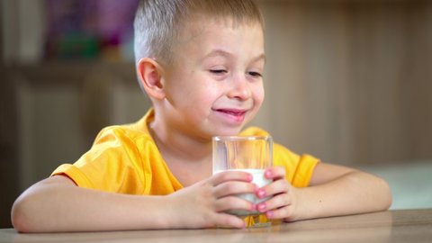 Boy holding a glass in her hands and drinks milk. Little boy drinks milk. Happy child has breakfast at home. Healthy child having breakfast.