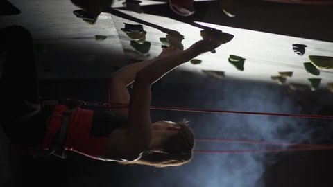 Woman climber training on a climbing wall, young woman practicing rock-climbing and moving up, vertical video, rises using insurance.
