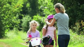 Mom helps two daughters put on a safe helmet before riding a bike on a Sunny summer day in nature and gives five to each other . Safety, sports, recreation. 4k video.