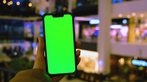 4k Chroma key. Close up of woman hand holds smart phone with green screen at shopping mall store. Shopping center. Department store. Shopping online. Gadgets template