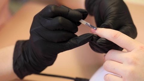 Manicure process in a beauty salon. The manicurist paints the nail with varnish.