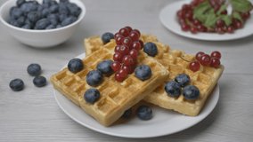 The chef puts a mint leaf on a plate of maple syrup-poured waffles garnished with berries. food video. Delicious dessert on a white plate
