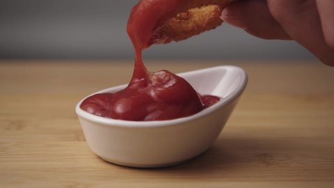 Onion rings is Dipped into a Ketchup Bowl on a Table with wooden Background a Macro Shot