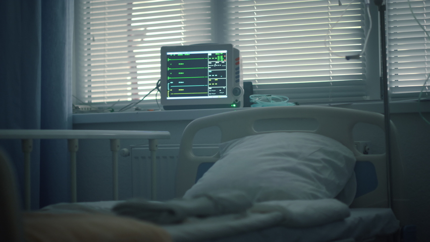 Heartbeat monitor at bed head in intensive care unit. Medical equipment in room. No patient in dark empty hospital ward with shuttered windows drip. Contemporary healthcare service business concept. Royalty-Free Stock Footage #1088740155