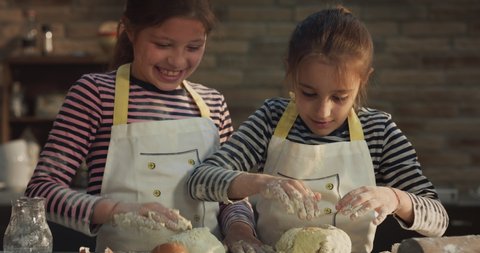 Cinematic authentic shot of happy little girls sisters are having fun to play together with dough of flour made by their mother for baking cookies in kitchen at home.
