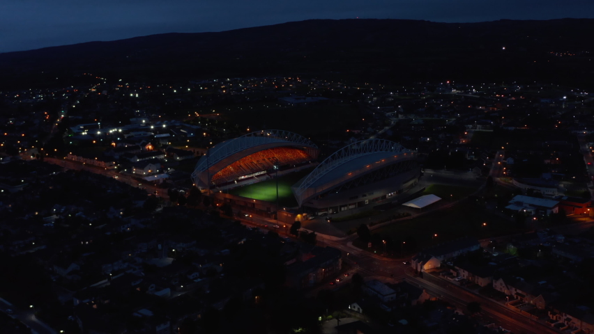 Slide and pan footage of light show and turning on main lights on football stadium. Aerial shot of sport centre in city at night. Limerick, Ireland
