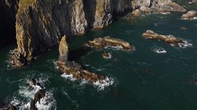 closed and static shot of waves impacting on rocks of the atlantic ocean in drone flight with a bluish sea. Cooper coast, ireland