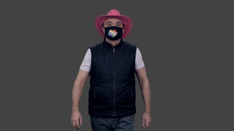 Gay man in pink cowboy hat and anti covid lgbt mask walking and sending air kisses to everyone, 4k footage with alpha transparency channel isolated on gray background