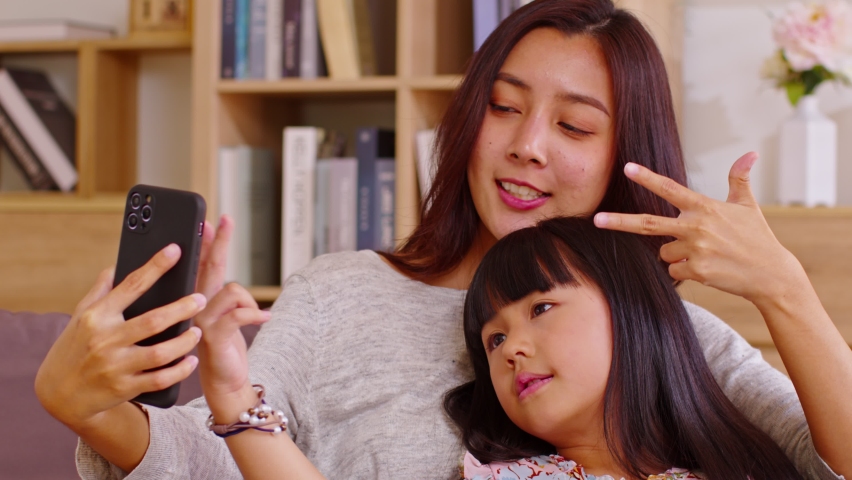 Asian mom and her kid are calling on smartphone. Both happy using cellphone for video call smiling mom and girl having fun greetings online with making video call communication through application.