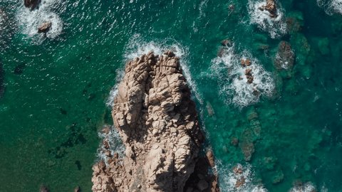 Drone aerial shot, ocean waves crashing on rocky shore. Cliff drop view