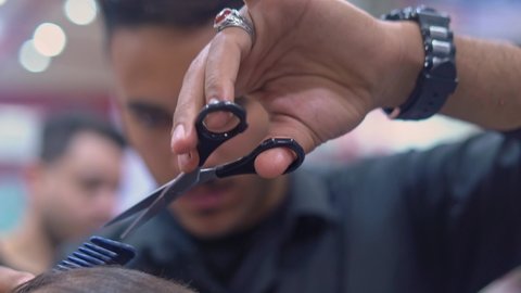 Close-up of hair cutting in the salon. Young Arab barber cuts man's hair with scissors in a barbershop.