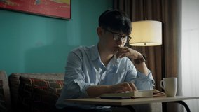 Tired office employee takes off glasses, resting from desk book work. Young attractive asian vietnamese man is busy working learning on desk book at home data analyst, data science scientist business.