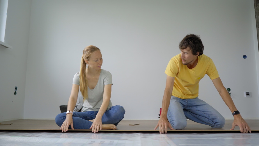 A family of woman and man install laminate on the floor in their apartment. DIY concept