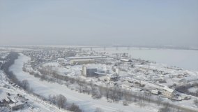 Aerial view of a frozen small city in winter season. Clip. Flying above snow and ice covered river and a town.