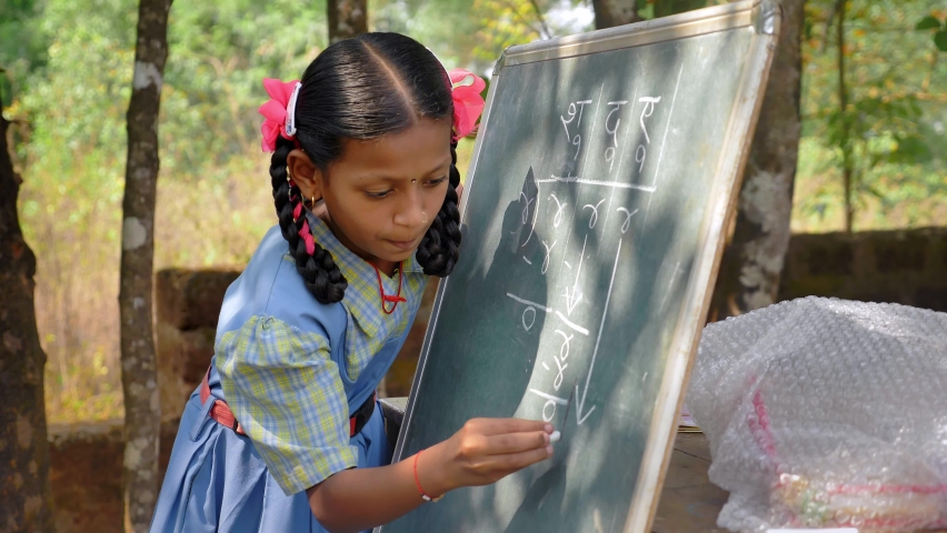 Indian Rural primary school girl wearing uniform writing or solving a mathematical problem or sum on a board with chalk standing outdoor in premises. Writing S, D, A, and number 4, 1, 0 in Marathi Royalty-Free Stock Footage #1088754471