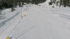 Aerial view of a ski resort with people snowboarding and skiing from a hill. Video footage. Flight over ski or snowboard track on white snow surrounded by thick forest