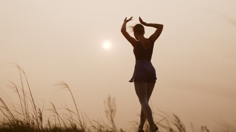 Young beautiful woman ballerina is dancing outside against sky, front view. Female dancer performs movements in preparation for performance