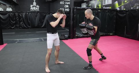 Beograd, Serbia - Feb 25th, 2022. Strong teenager training with foot mitts punching bag in mma gym. Extreme combat sports, young male aggressive fighter punching kick pad preparing for a fight