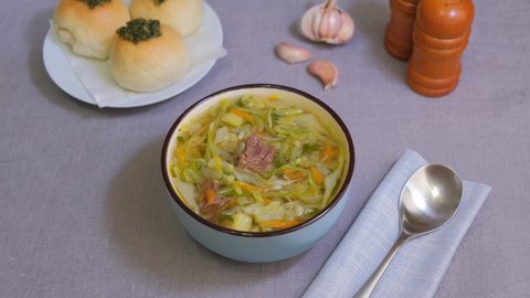Shchi with pampushki (buns) and lard. Soup of cabbage, potatoes and meat. Traditional Russian and Ukrainian cuisine. Woman puts parsley in her soup. Close-up.