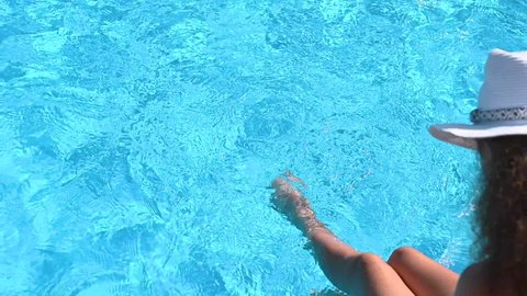 Young  women wetting feet in swimming pool. Relaxed girl resting at summer resort on sunny day. Top view of beautiful clear blue water.