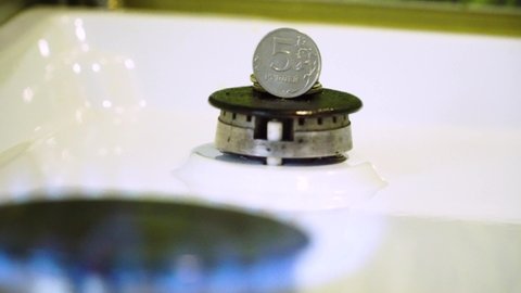 Gas burner on which there is a Russian ruble. The coin of the Russian ruble is shown with the front side. There are several coins on the burner