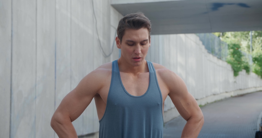 Portrait of handsome strong young man. Healthy athletic fitness model looking at camera, standing outdoors at stadium. 