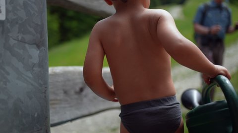 Child wearing underwear during summer day holding watering can outside