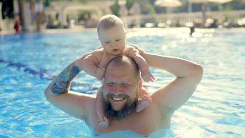 Cute baby having swimming lesson with his mother and father. Healthy family teaching their baby to swim in the swimming pool. Young father takes his son and embraces him while the kid is smiling
