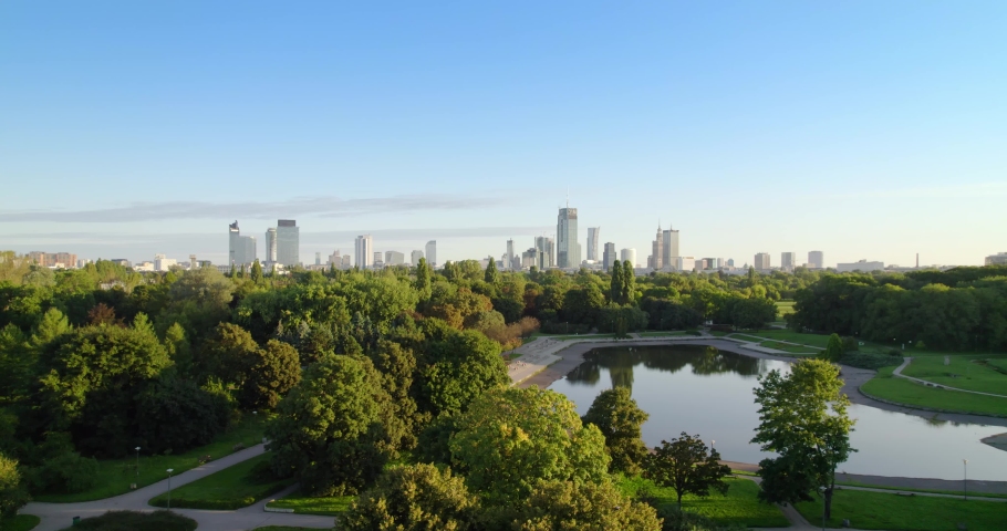 City park with the city center in the background. Aerial view of offices in skyscrapers over the panorama of Warsaw in a urban park. Lake in the park with green trees during summer. Royalty-Free Stock Footage #1088759699
