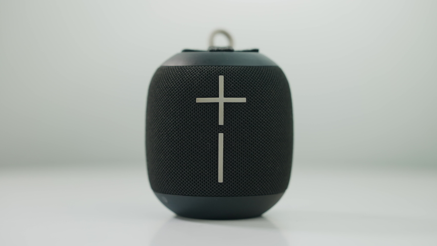 Close-up black portable speaker with female hand pressing plus sign adding volume. Unrecognizable Caucasian young woman listening to music enjoying hobby at white background