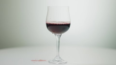 Close-up glass on white table with red wine or juice pouring spilling. Filling drinking glass with liquid drink at white background