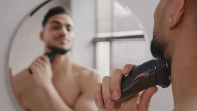 Mirror reflection handsome indian arabian caucasian spaniard bearded man guy shaves beard with trimmer electric razor shaving at home bath morning beauty routine male face facial grooming in bathroom - Powered by Shutterstock - Get 15% off with code: PIKWIZARD15