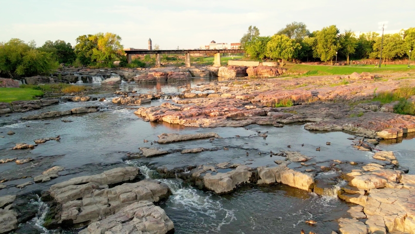 Falls Park South Dakota. Water flowing and falling over the stones. Ducks swimming in the water. Sun shining through the shadows and gleaming off the rocks and water. Cloudy sky. 