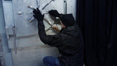 A bank robber breaks into a bank vault and opens the safe door.