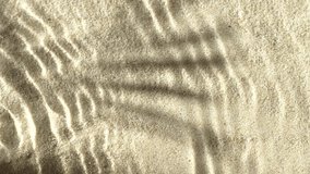 Slow motion water surface ripples and splash with palm tree leaf shadow on sand 
